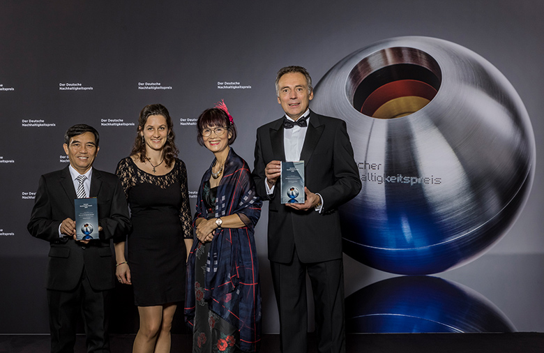Vier Personen posieren vor dem Symbol des Deutschen Nachhaltigkeitspreises für die Kamera.